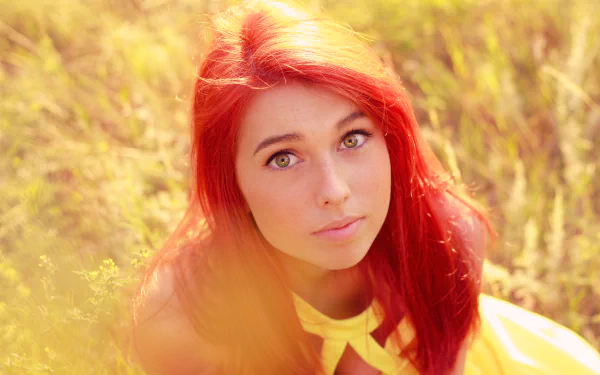 A close-up of a woman with striking red hair and captivating green eyes, softly framed by warm, golden background hues. This HD image serves as a vibrant desktop wallpaper.