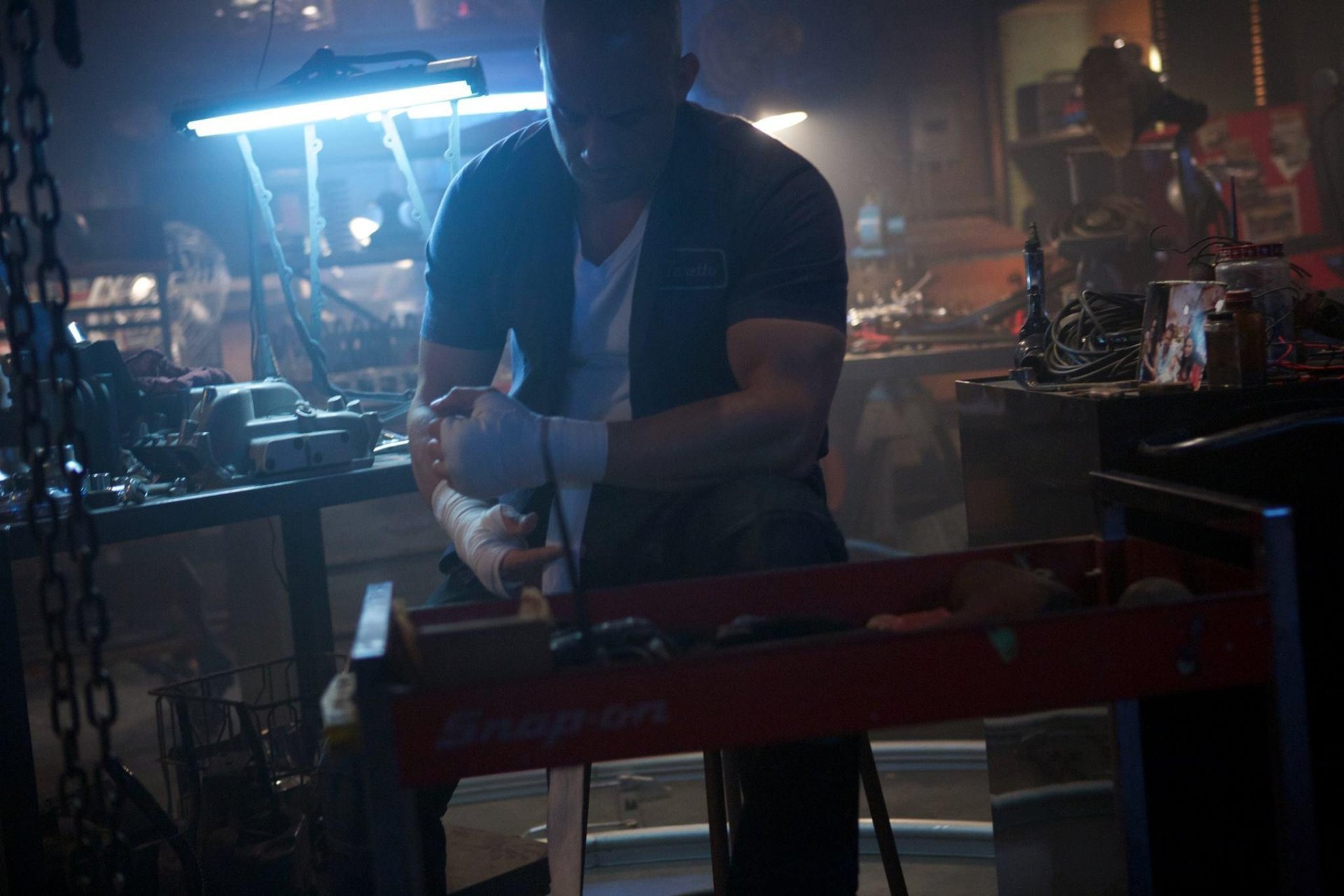 Dominic Toretto, portrayed by Vin Diesel, works intently in a dimly lit garage filled with tools and equipment, capturing the gritty essence of Furious 7 in this HD wallpaper.
