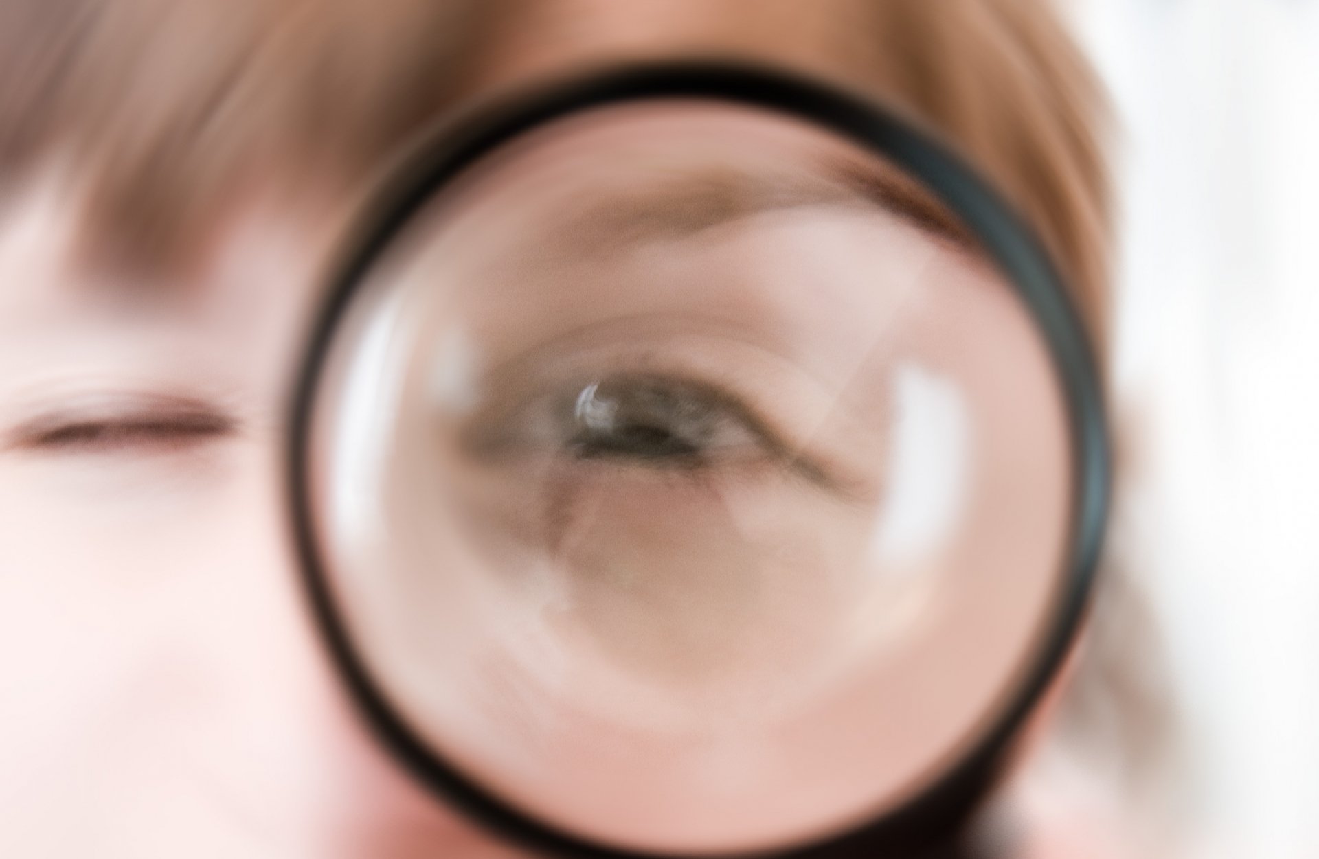 Artistic human close-up: blurred face seen through a magnifying glass enlarging one eye, soft neutral tones — 2K Quad HD PC desktop wallpaper and background.