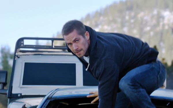 Brian O'Conner, played by Paul Walker, climbs onto a vehicle in a thrilling scene from Furious 7, showcasing action and adventure in this HD desktop wallpaper.