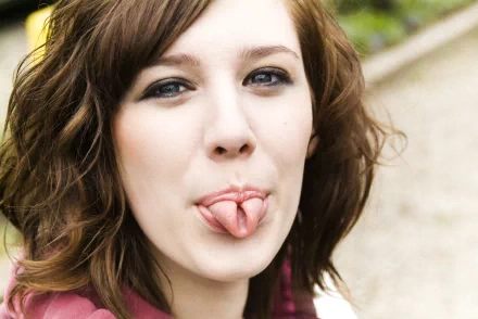 A playful woman with curly brown hair is sticking out her tongue, capturing a goofy moment. This HD image serves as an engaging desktop wallpaper and background.