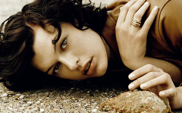 HD PC desktop wallpaper featuring a close-up portrait of celebrity Milla Jovovich lying on a textured surface, showcasing her intense gaze and natural beauty.