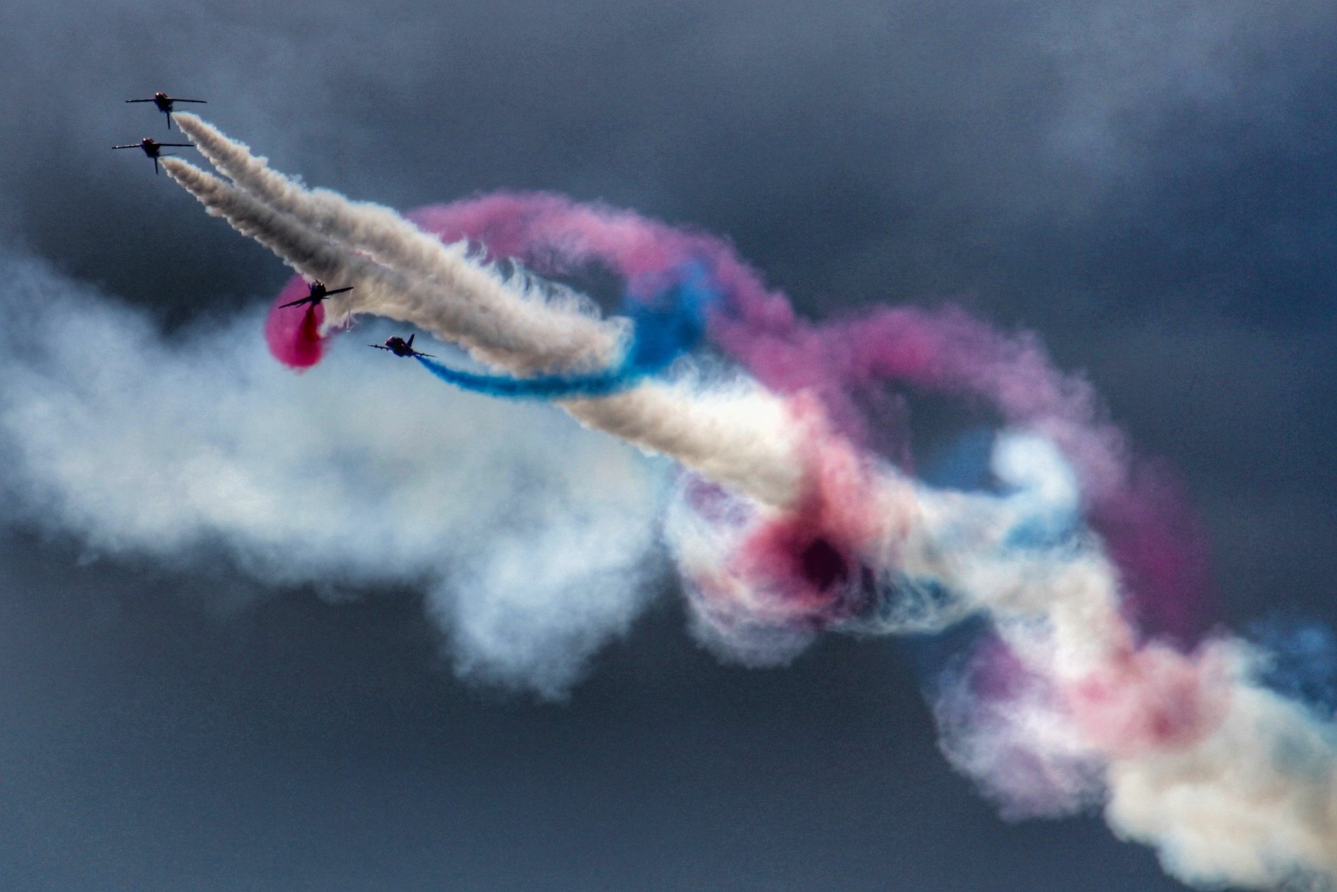 2K Quad HD PC Desktop Wallpaper and Background of military jets at an air show carving red, white and blue smoke trails across a brooding sky.