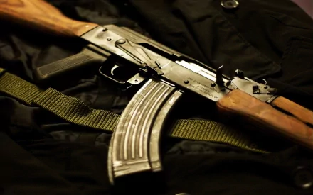 High-definition desktop wallpaper featuring an AKM assault rifle with wooden elements, resting on a black fabric background with a green strap.