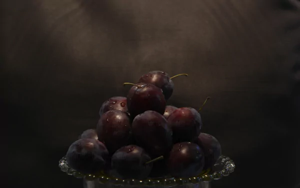 5K Ultra HD PC desktop wallpaper: food still-life of glossy dark plums piled on a glass plate, moody spotlight and deep-shadow background.