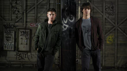 Two characters from the TV show Supernatural stand confidently in an urban setting with graffiti on the walls, showcasing a moody atmosphere. HD desktop wallpaper background.
