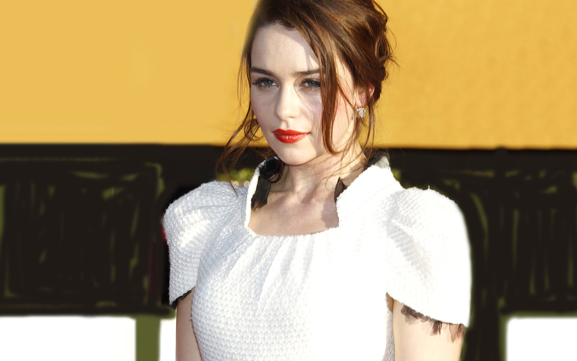 Close-up of Emilia Clarke in a stylish white dress, presenting a confident look with red lips. A vibrant background enhances the HD desktop wallpaper's appeal.