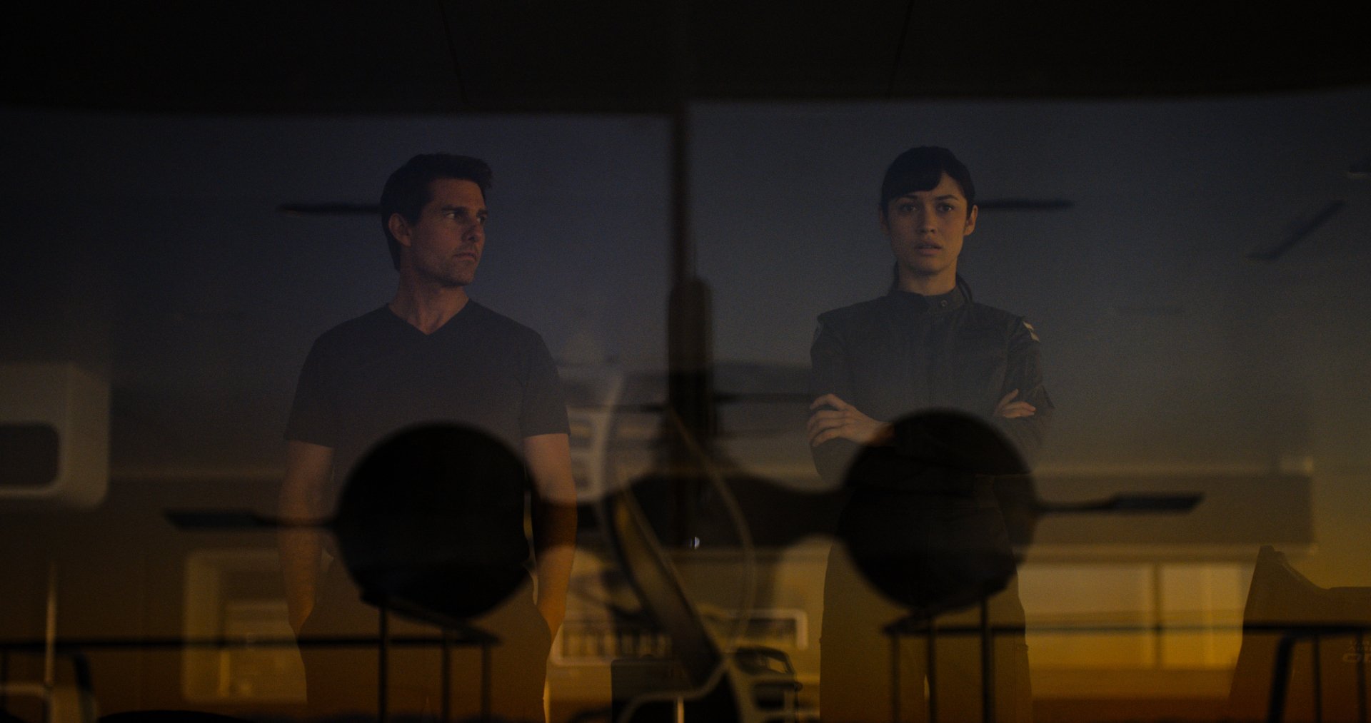 A dramatic image from the movie Oblivion, featuring Tom Cruise and Olga Kurylenko, set against a backdrop with silhouettes of aircraft, highlighting a tense moment in a sci-fi landscape.