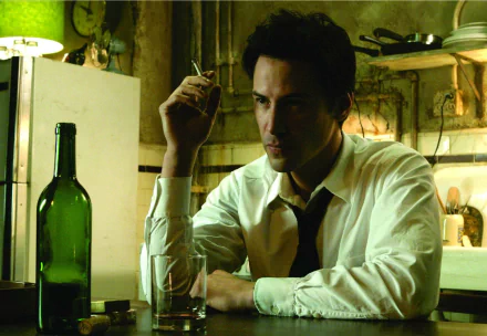 Keanu Reeves as John Constantine sits at a dimly lit table, holding a cigarette, with a glass and a green bottle nearby, capturing a moody moment from the movie Constantine.