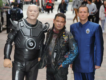 HD PC desktop wallpaper of three Red Dwarf TV show characters posing together: a silver-armored robot, a patched leather-clad man, and a blue-uniformed crewman.