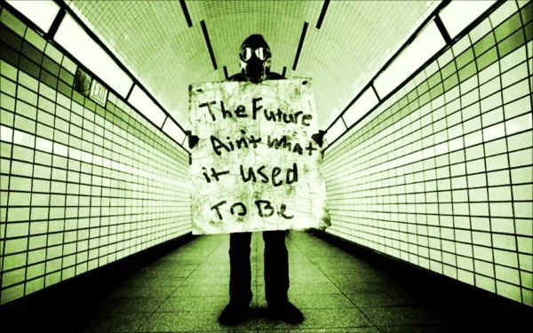 A Sci-Fi, post-apocalyptic HD wallpaper depicts a person in a gas mask holding a sign that reads, The Future Ain't What It Used To Be, standing in an eerie, tiled hallway.