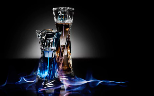 A striking HD wallpaper featuring two elegant perfume bottles—one blue and one brown—surrounded by soft blue flames against a dark background. A captivating blend of photography and fragrance.