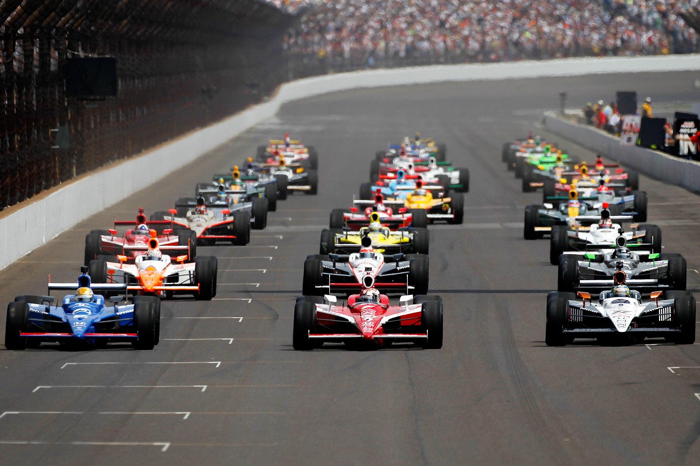 HD PC desktop wallpaper and background: F1 sports scene — rows of open-wheel race cars charging from the start line on a wide oval track with packed grandstands.