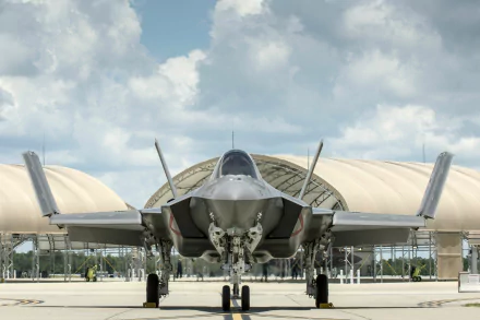 HD desktop wallpaper featuring a Lockheed Martin F-35 Lightning II military jet parked on a runway with hangars and a cloudy sky in the background.