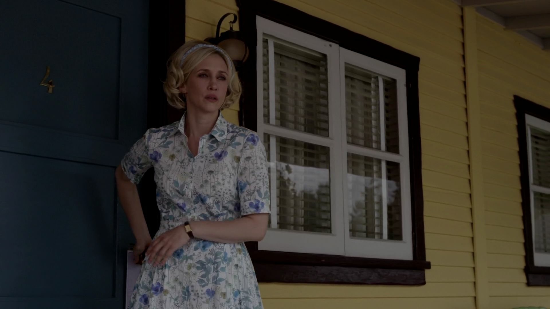 Vera Farmiga stands outside a yellow house in a colorful floral dress, capturing a moment from the TV show Bates Motel in this HD desktop wallpaper.