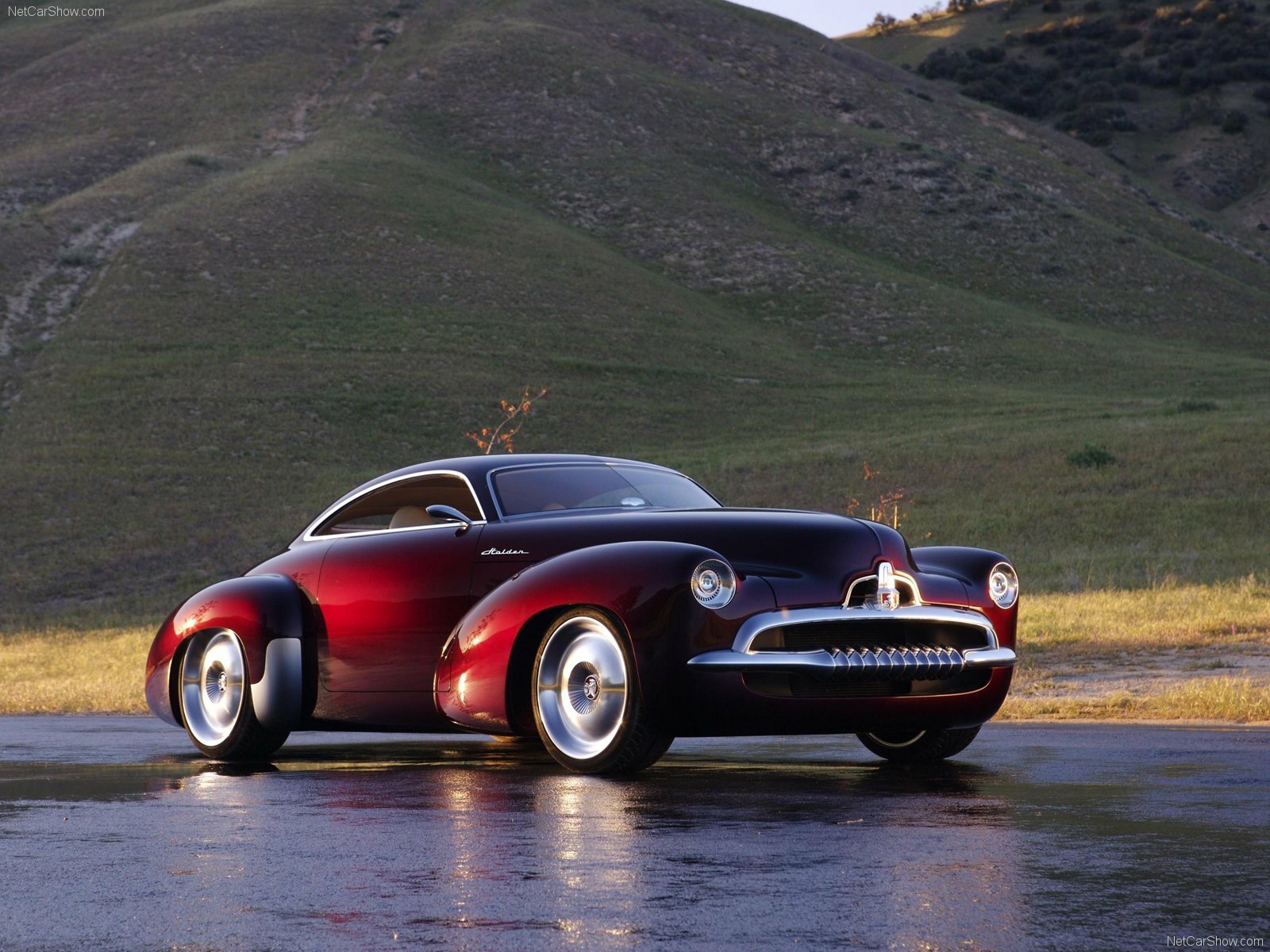 HD PC desktop wallpaper of glossy maroon Holden Efijy concept car on wet pavement with rolling green hills behind.
