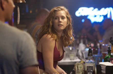 Amy Adams in a scene from the movie The Fighter, set in a lively bar environment. The image captures her thoughtful expression amidst a vibrant background.