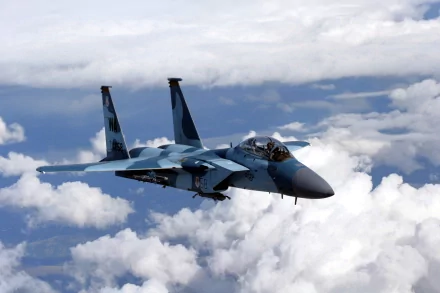 HD desktop wallpaper featuring a McDonnell Douglas F-15 Eagle military jet flying above white clouds against a blue sky.