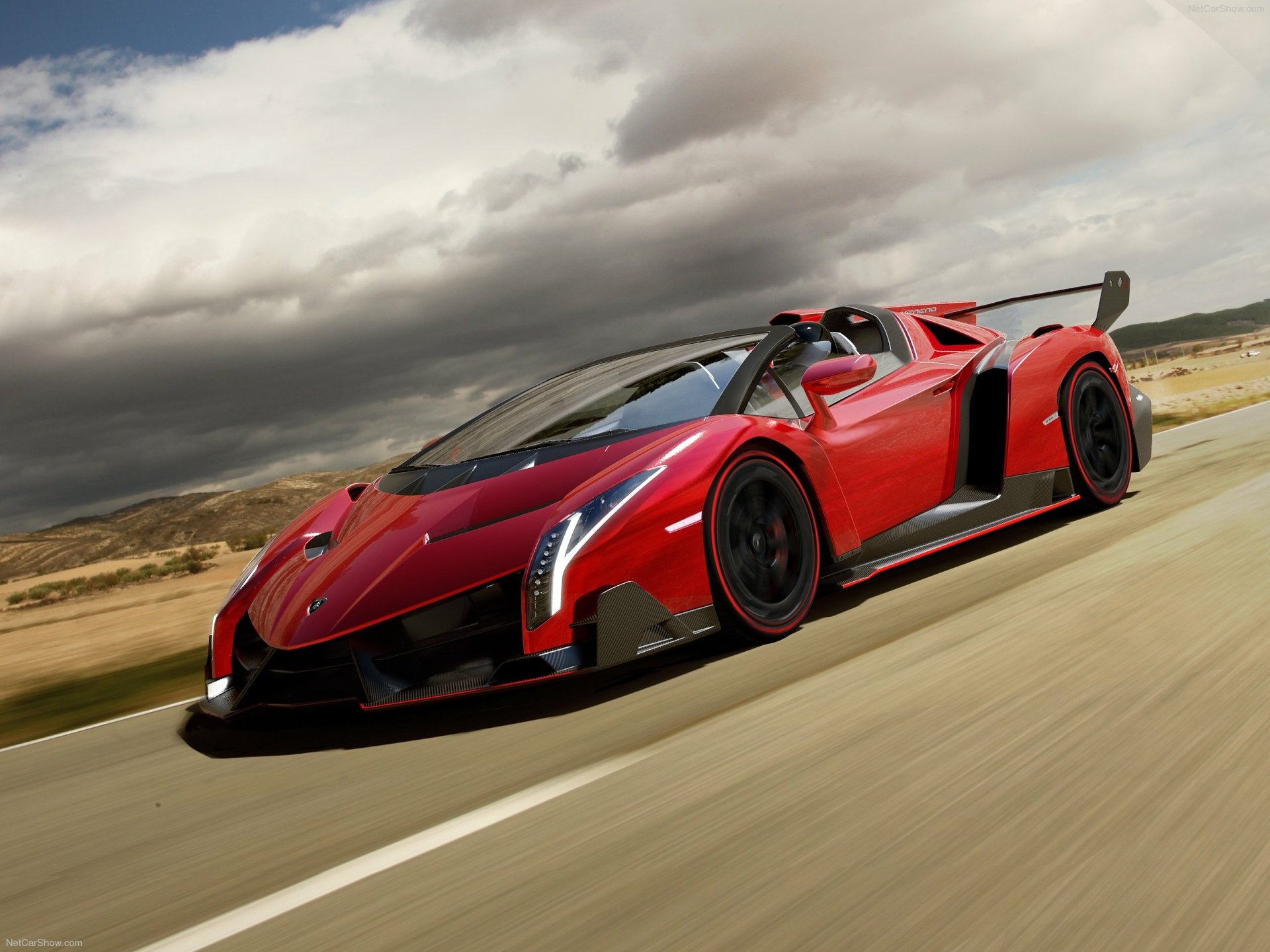 HD desktop wallpaper featuring a sleek red Lamborghini Veneno Roadster racing along an open road under a dramatic, cloudy sky.