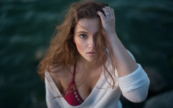 A stunning brunette model with freckles and blue eyes gazes intently at the camera, framed by a blurred natural backdrop in this captivating 4K Ultra HD wallpaper.