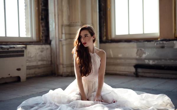 Brunette model with freckles, brown eyes and red lipstick sits in a flowing white dress in a sunlit, weathered room — 8K Ultra HD PC desktop wallpaper and background.