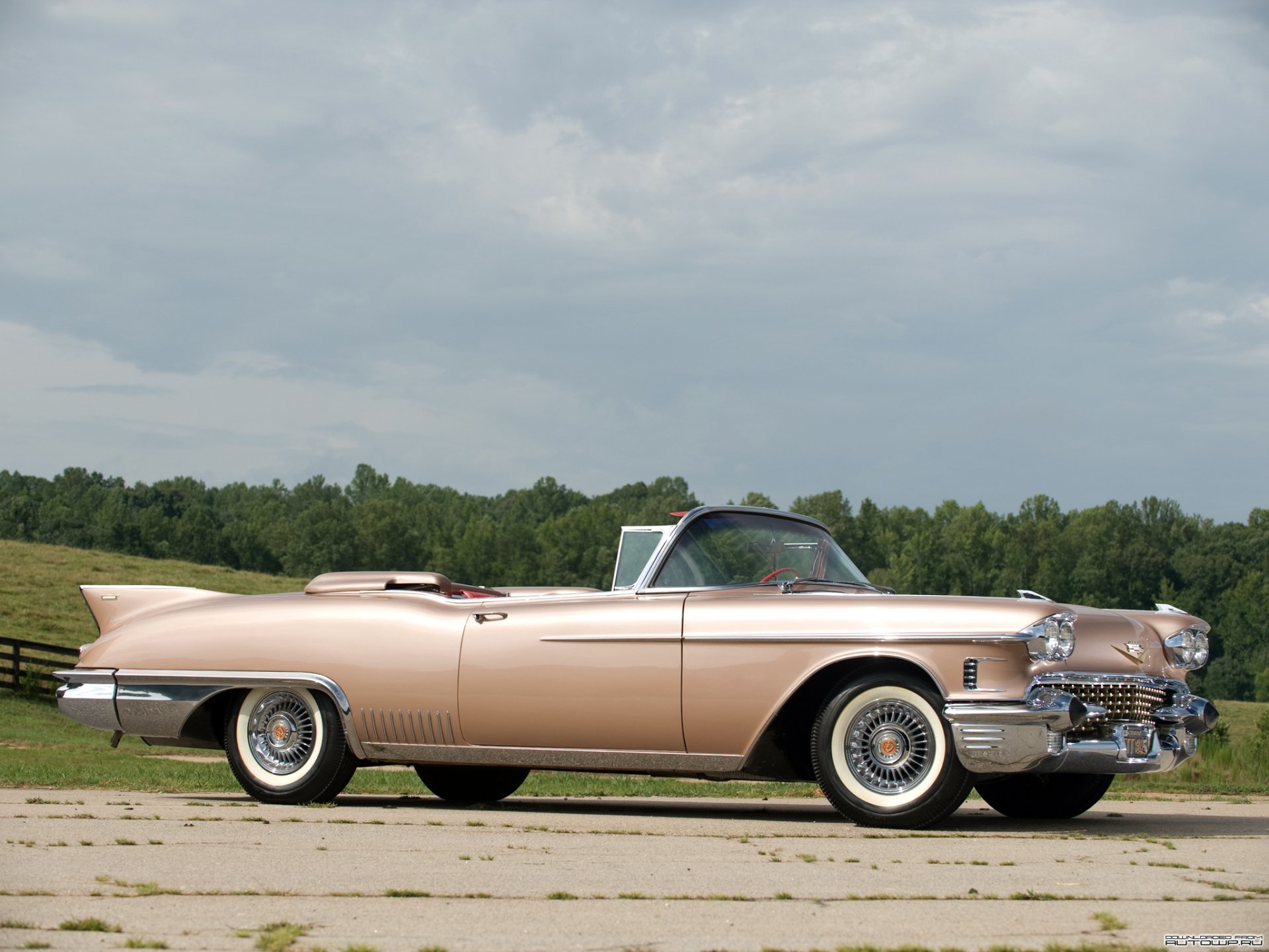 A classic Cadillac Eldorado convertible in a soft pink hue, captured outdoors with a cloudy sky and green landscape, featured as an HD PC desktop wallpaper.