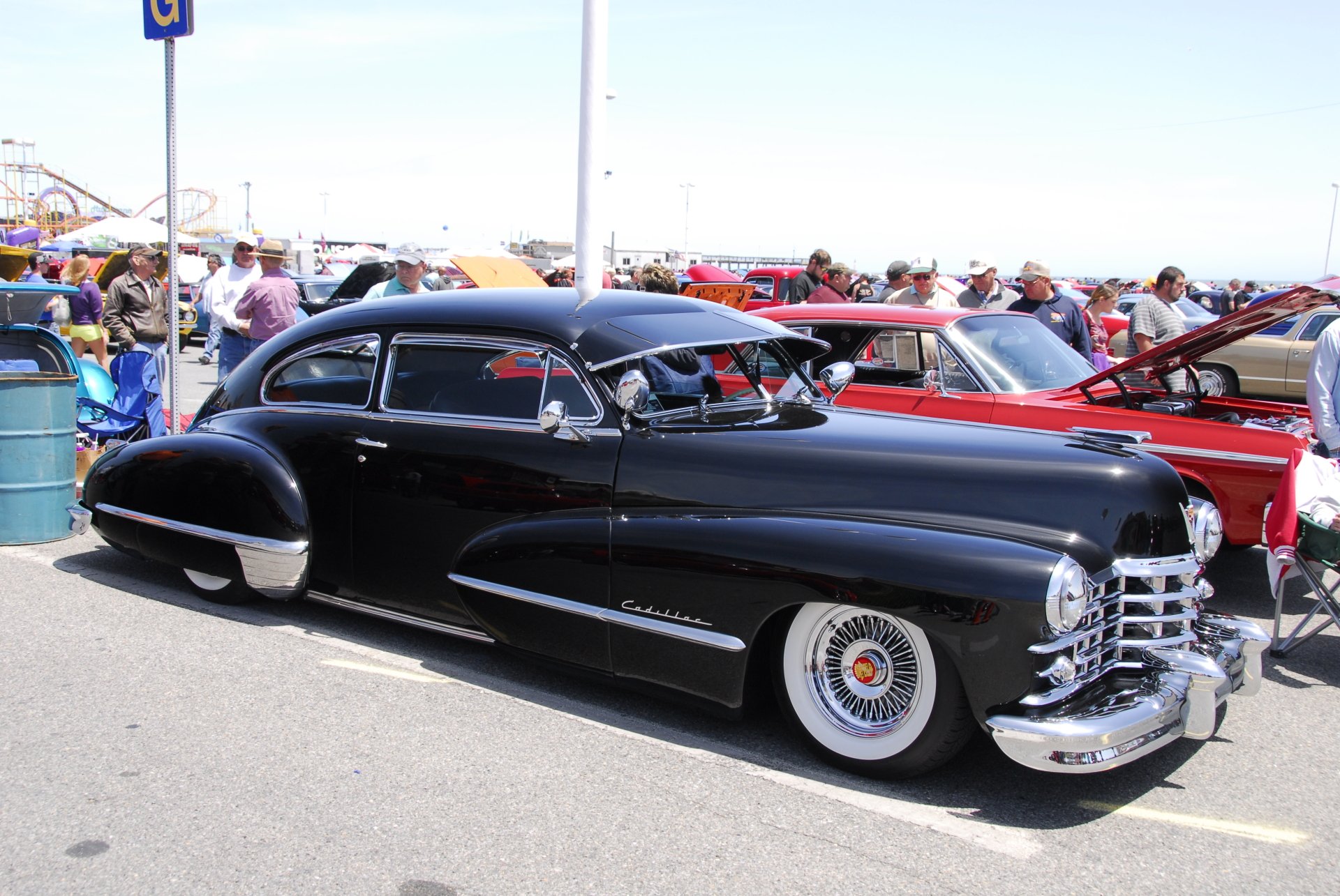 4K Ultra HD PC desktop wallpaper: sleek black Cadillac Series 62, low-slung profile with whitewall tires and gleaming chrome, parked at an outdoor car show.