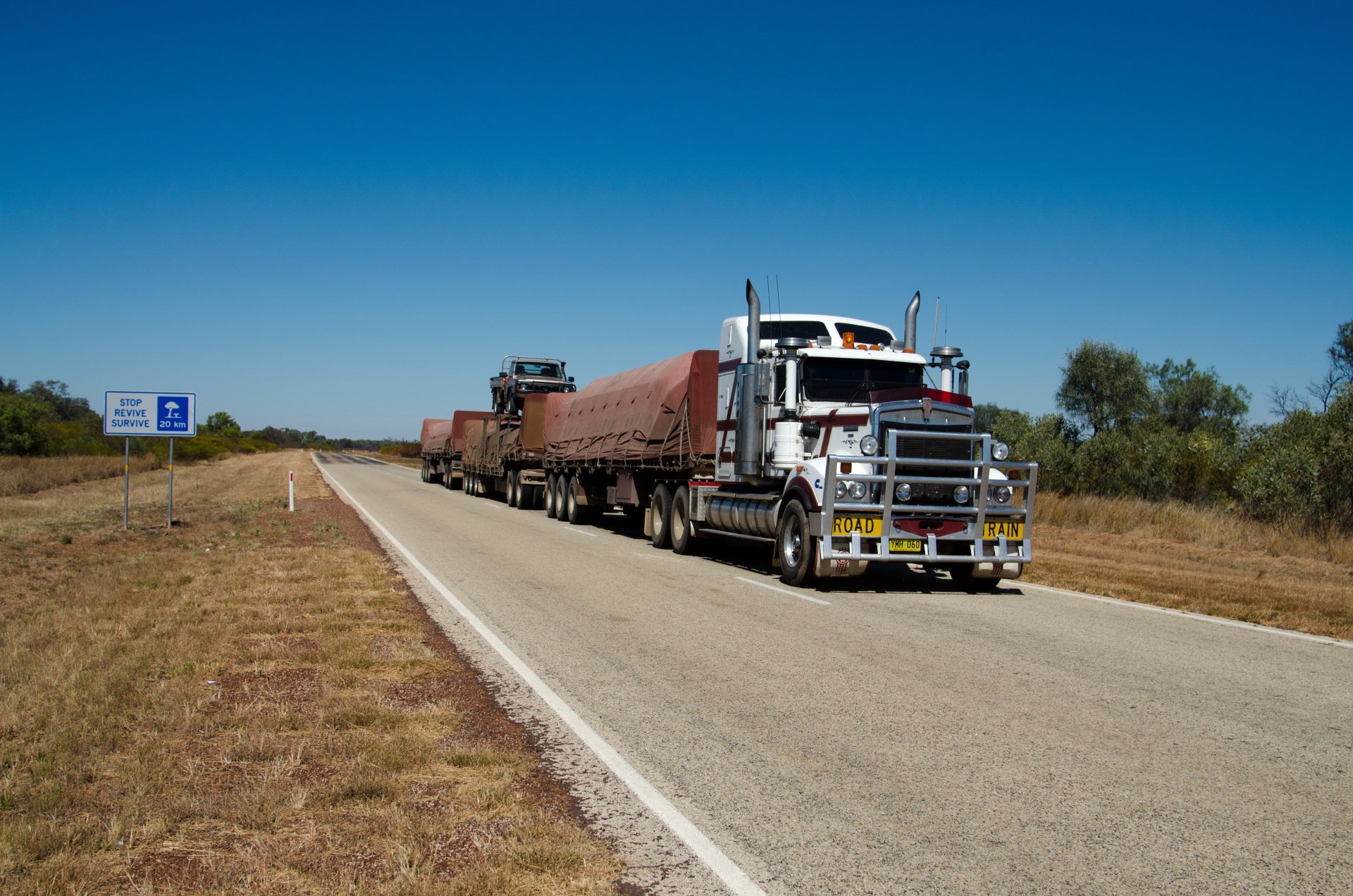 A Kenworth truck hauling cargo on a rural highway under a clear blue sky, captured in 4K Ultra HD as a PC desktop wallpaper and background.
