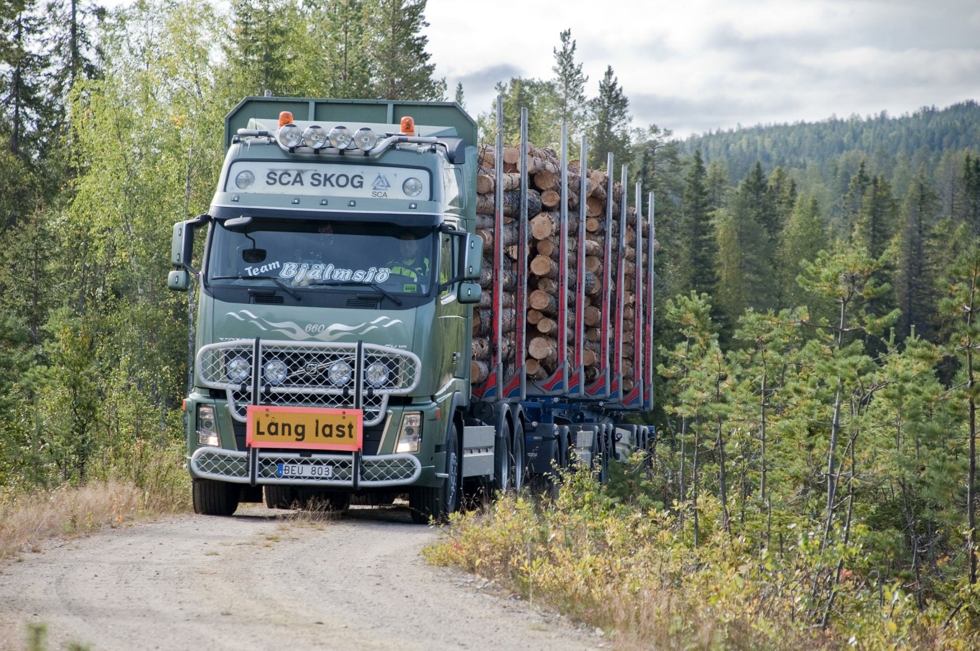 Volvo logging vehicle loaded with timber on a forest road — 2K Quad HD PC desktop wallpaper/background.