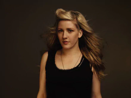 A captivating HD desktop wallpaper featuring Ellie Goulding, showcasing her in a striking portrait with flowing hair and a stylish black outfit against a dark background.