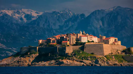 HD PC desktop wallpaper: Calvi, Haute-Corse man-made fortified citadel on a rocky promontory above blue sea, rugged Corsican mountains behind.