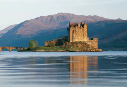 HD desktop wallpaper showcasing the man-made Eilean Donan Castle surrounded by calm water with mountains in the background.