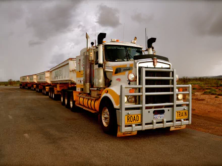 A powerful Kenworth road train stands on a wide, open road, showcasing its impressive design and heavy-duty capabilities against a dramatic sky, making an impactful HD desktop wallpaper.