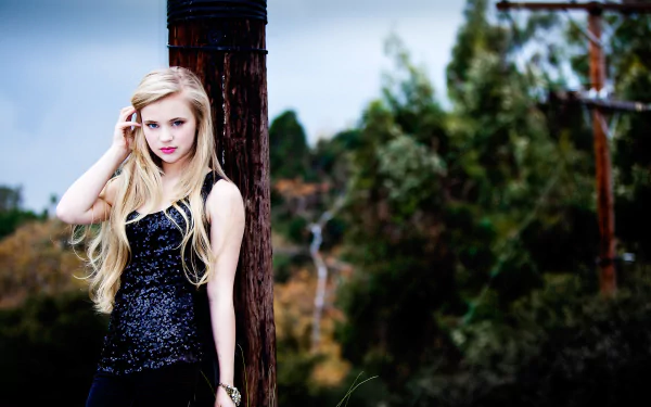 HD PC desktop wallpaper featuring woman Sierra McCormick with long blonde hair, wearing a black sequined dress, standing outdoors against a wooden post with greenery in the background.
