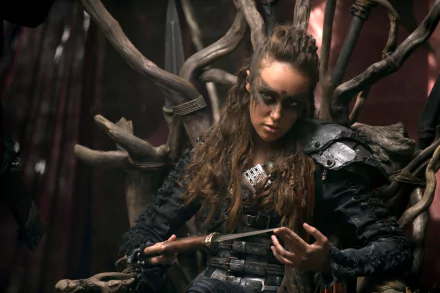 Alycia Debnam-Carey as her character in The 100, dressed in post-apocalyptic warrior attire, sitting on a throne-like structure, holding a knife. HD desktop wallpaper and background.