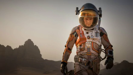 HD desktop wallpaper featuring Matt Damon in a spacesuit from the movie The Martian, set against a rocky, mountainous Martian landscape at dusk.
