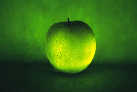 HD desktop wallpaper featuring a glowing green apple against a matching green background, highlighting the fruit's texture and vibrant color.