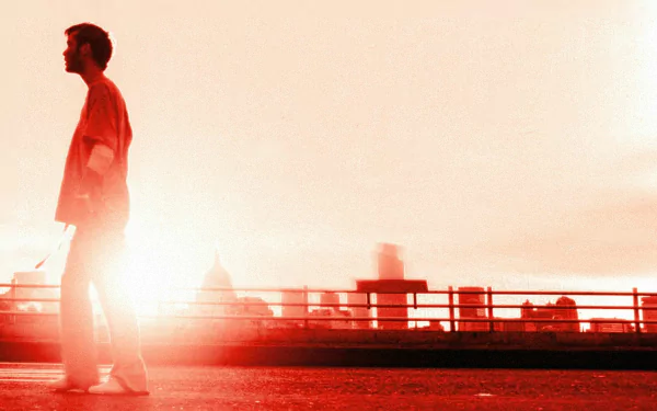 28 Days Later movie HD PC desktop wallpaper/background: lone silhouetted man on an empty bridge against a blinding red-orange sunrise with a distant, washed-out urban skyline.