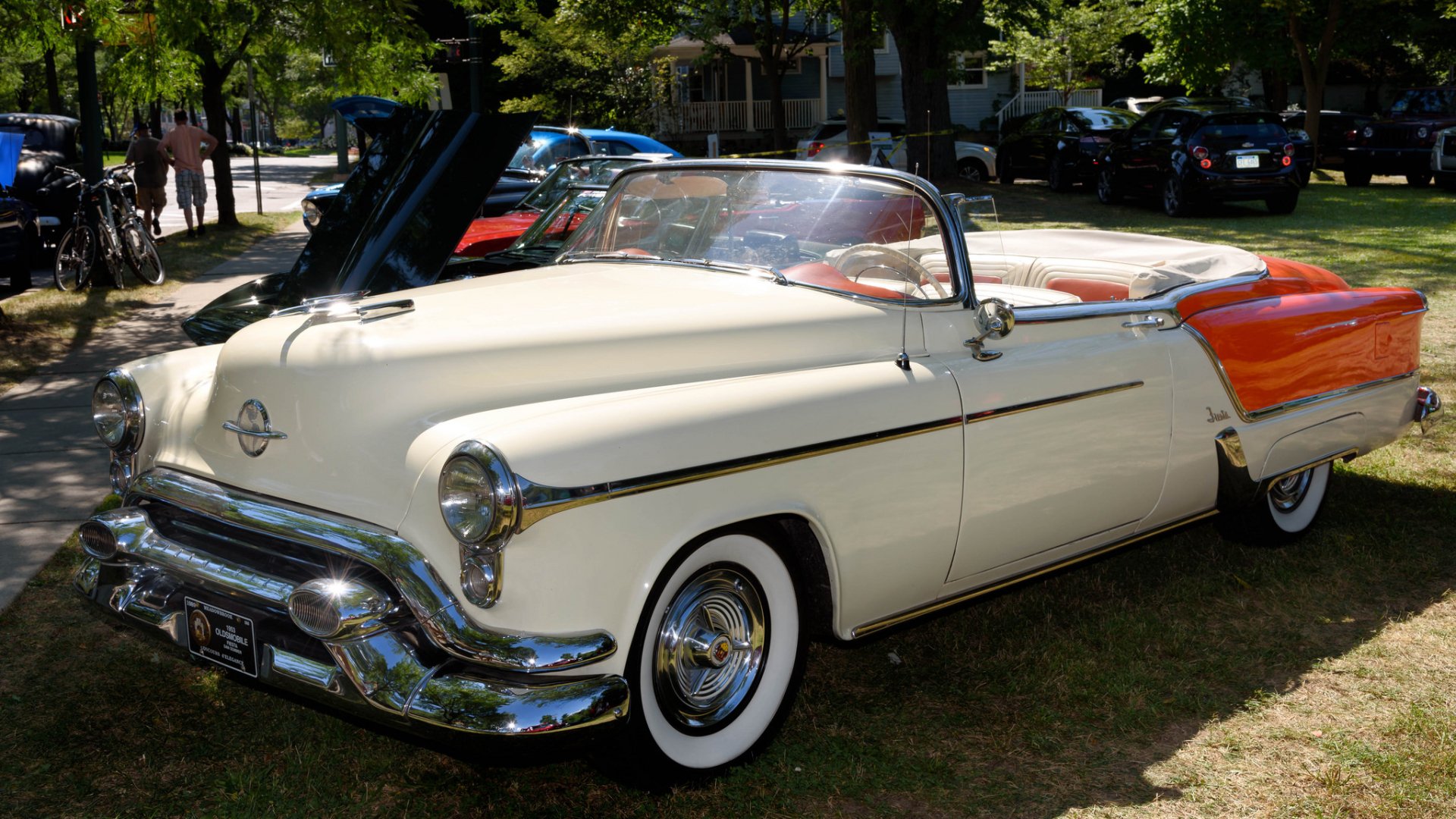 1953 Oldsmobile Ninety-Eight Fiesta Convertible parked on grass, showcasing classic design with cream and orange paint in a sunny outdoor setting.