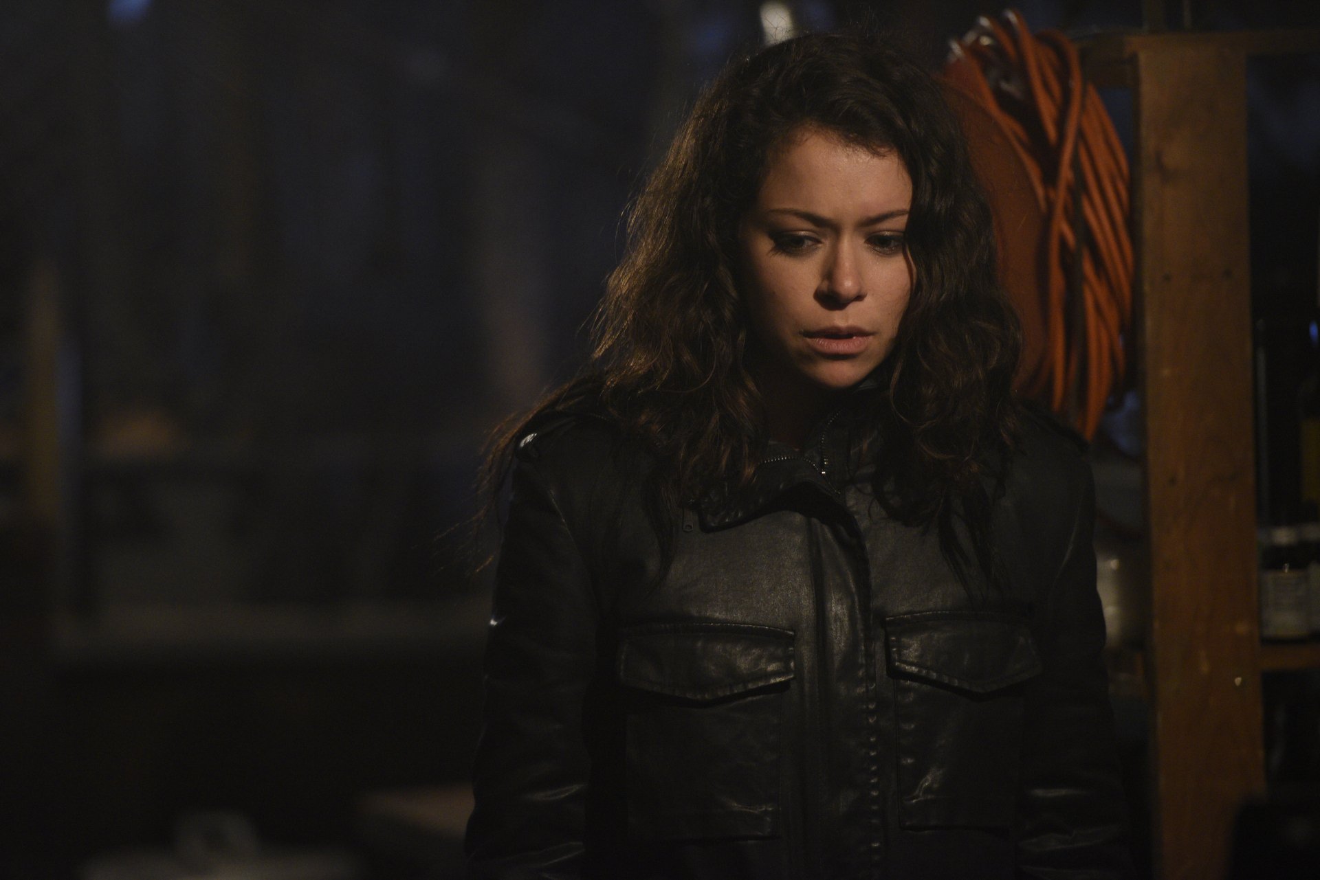 4K Ultra HD PC desktop wallpaper from the TV show Orphan Black: a tense, brooding woman in a dark jacket stands in a dimly lit storage space.
