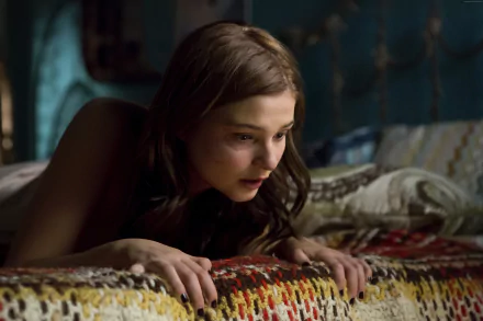 A scene from Insidious: Chapter 3 featuring Stefanie Scott. The image captures her in a tense moment, leaning forward with an intense expression against a colorful patterned background.