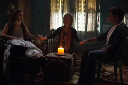 A scene from Insidious: Chapter 3 featuring Stefanie Scott, Lin Shaye, and Dermot Mulroney, as they engage in a tense moment around a candle in a dimly lit room.