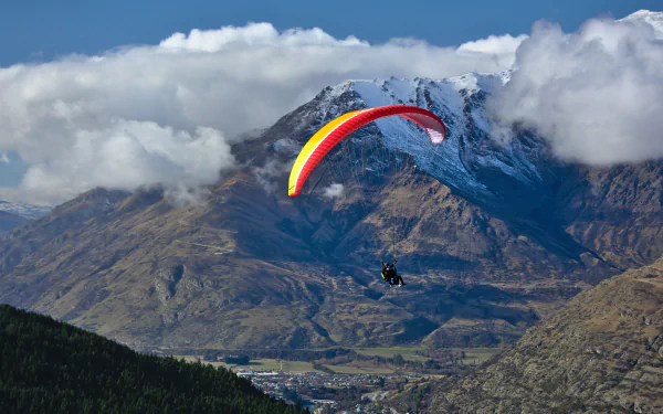 A tandem paraglider soars over rugged mountain landscape under a partly cloudy sky, captured in stunning 4K Ultra HD for a vivid sports wallpaper.