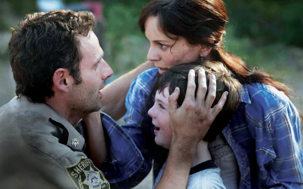 A dramatic scene from The Walking Dead featuring Rick Grimes (Andrew Lincoln), Lori Grimes (Sarah Wayne Callies), and Carl Grimes (Chandler Riggs) expressing intense emotions.