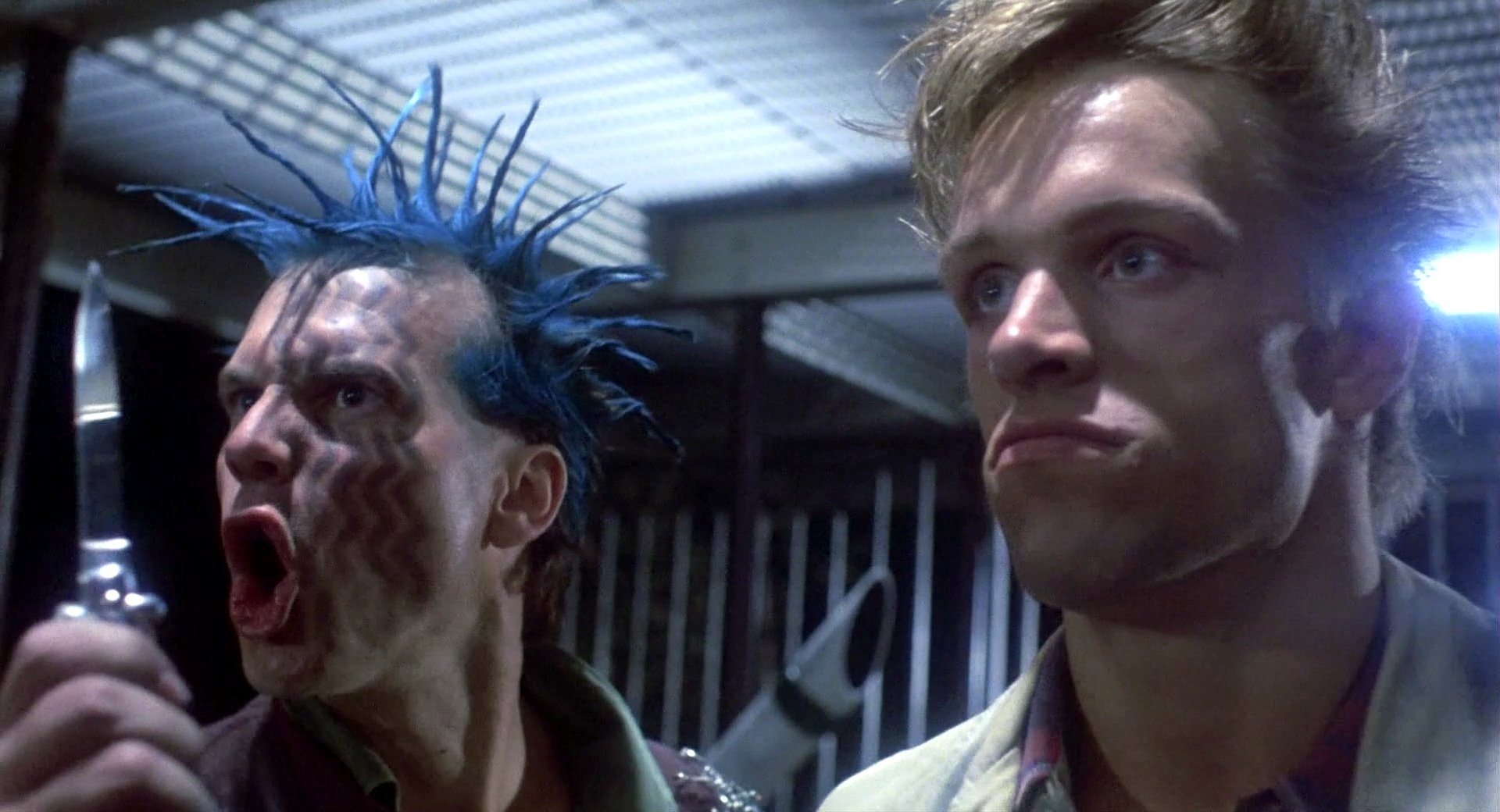 A scene from the movie The Terminator featuring two intense characters, one with blue spiked hair and the other looking stern, captured in high-definition for a dramatic desktop wallpaper.
