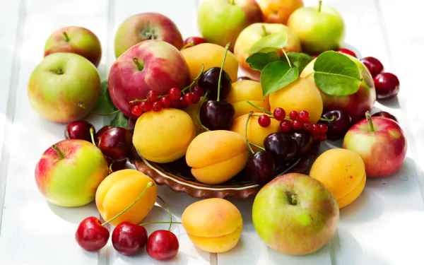 A vibrant assortment of cherries, apricots, apples, and berries arranged beautifully, showcasing a colorful display of fresh fruit on a light background.