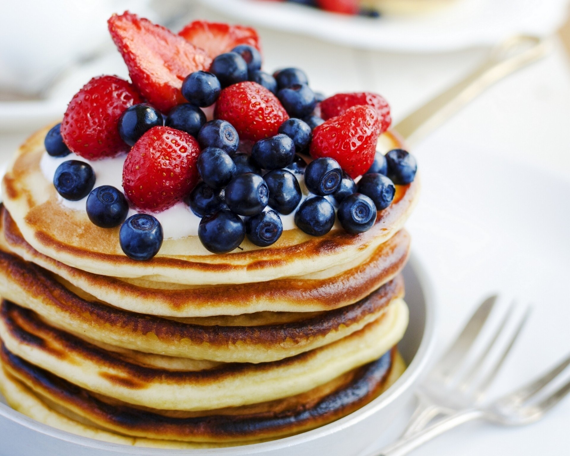 HD desktop wallpaper showing a stack of golden pancakes topped with fresh blueberries and strawberries, capturing a delicious breakfast moment.