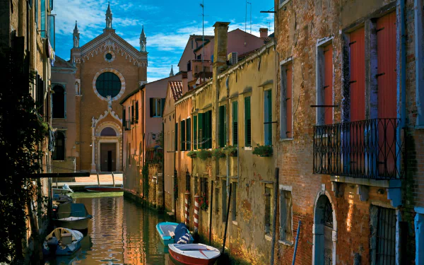 4K Ultra HD wallpaper of a man-made canal in Venice, Italy, lined with historic buildings and boats under a vibrant blue sky.