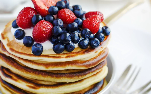 HD desktop wallpaper showing a stack of golden pancakes topped with fresh blueberries and strawberries, capturing a delicious breakfast moment.