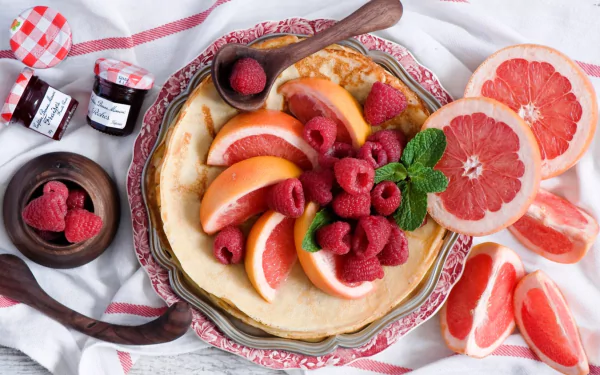 A vibrant breakfast featuring pancakes topped with raspberry jam, fresh raspberries, and grapefruit slices, styled as an HD PC desktop wallpaper.